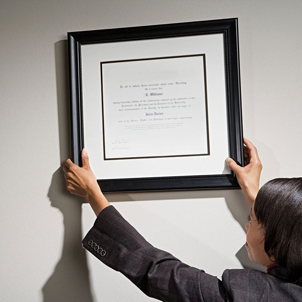 A smiling woman hanging a framed document on the wall