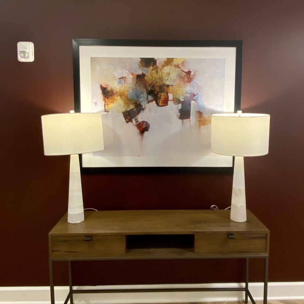 A framed abstract print hanging between two lamps