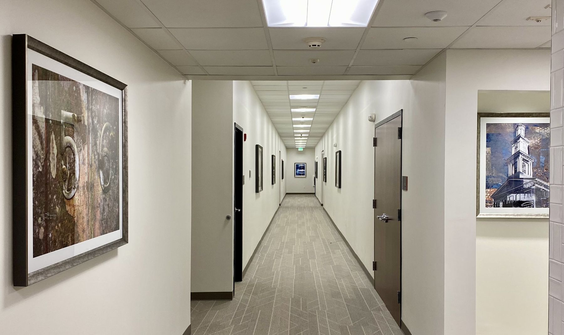 A hallway in a commercial building with several pieces of framed art hung on the wall